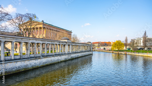 A serene view of the Old National Gallery located along the riverbank in Berlin, with classical architecture and clear skies. Germany