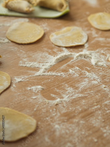 Preparing dumplings: A vertical close-up of circles of dough, spelt and whole wheat flour scattered across the table.