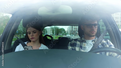 Couple driving in a car and fastening seat belts. Young lady using smartphone. Transport, travel, relationships, safety concept. Real time