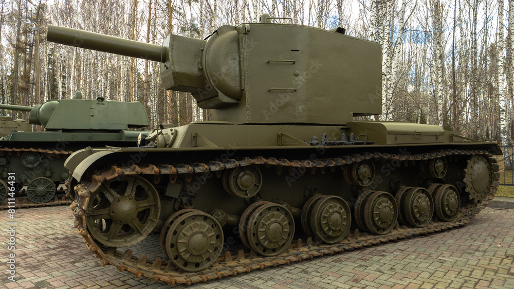 A large green tank with a black barrel sits in front of a forest