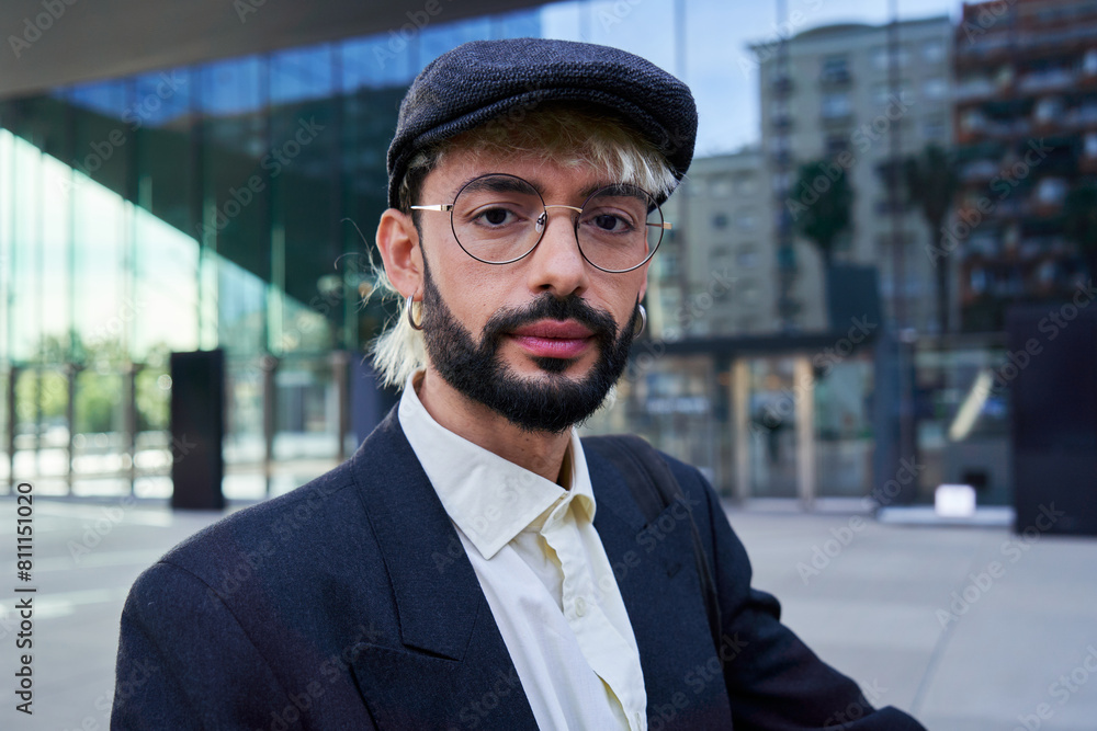 Portrait of a young hipster businessman looking at camera with a serious and confident face, wearing a beret hat, standing outside financial district. Portrait of a young hipster businessman looking at camera with a serious and confident face, wearing a beret hat, standing outside financial district.