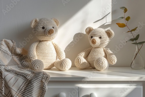 Handmade crochet teddy bear doll sitting on white drawer commode in baby room. Kid room interior, white walls with shadows and wooden furniture photo