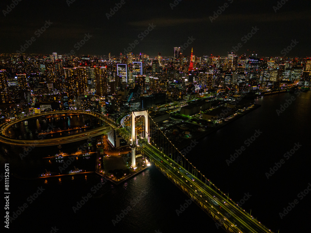 Naklejka premium Aerial view of a Rainbow Bridge in Tokyo with evening lights against a background of skyscrapers and lights of moving cars