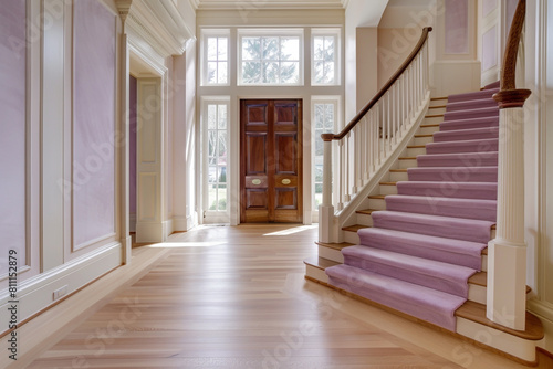 Luxurious entrance featuring a soft lavender staircase broad wooden front door and pale hardwood floors extending to a tall ceiling Gentle elegant design