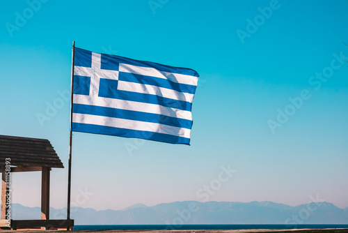 The national flag of Greece against the sky and mountains. Greece Independence Day. Waving Greek twocolor. Popularly referred to as the blue and white one. Popular tourist destination. Travel concept.