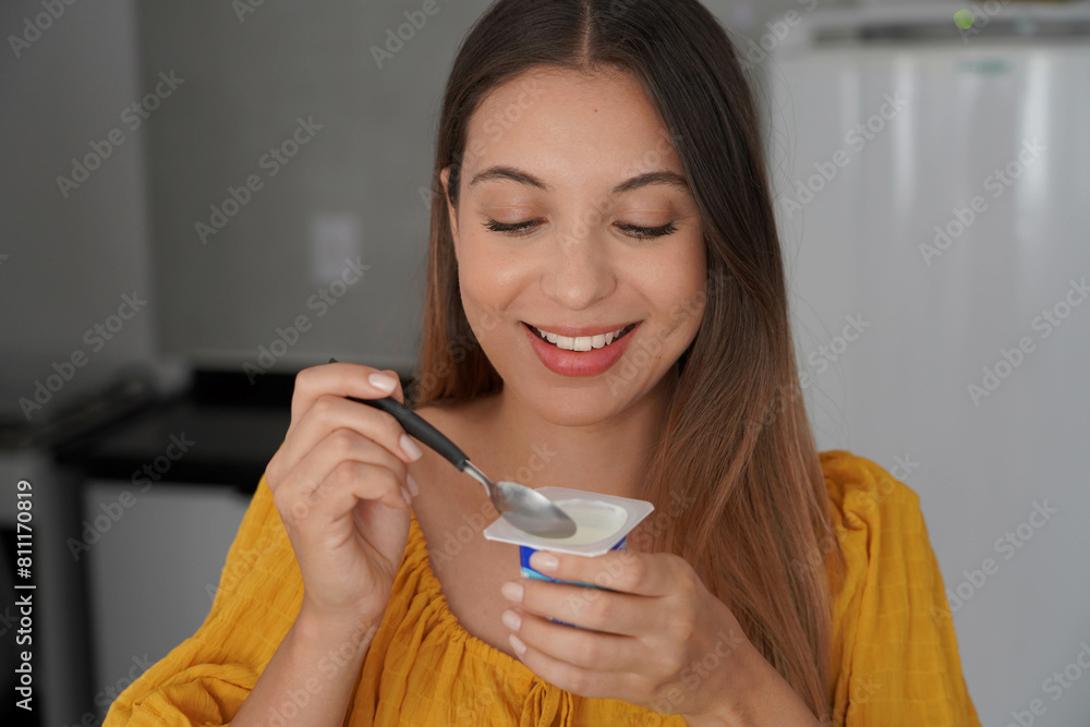 Hispanic cheerful young woman eating yogurt natural in the kitchen at home Hispanic cheerful young woman eating yogurt natural in the kitchen at home