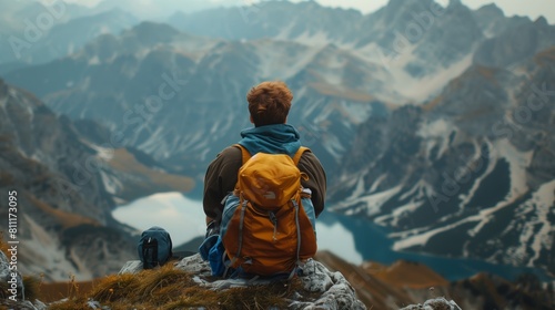 A lone traveler with a backpack sits at the peak of a mountain, overlooking the breathtaking view below