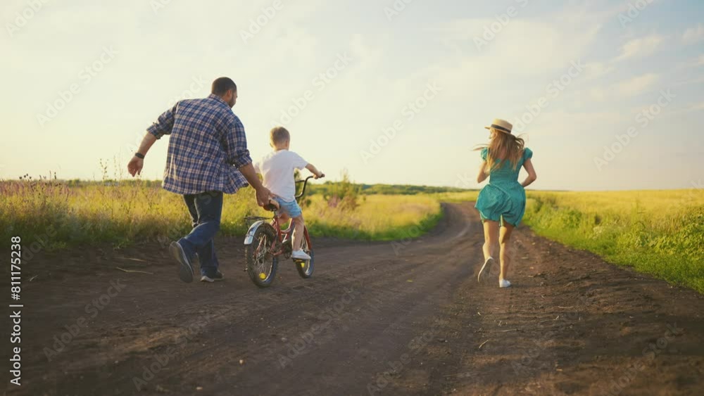 Mom dad teaching son ride bike together in village on summer vacation. Parents running near child boy father holding bicycle clapping hands supporting kid. Family weekend on nature, young adult. Mom dad teaching son ride bike together in village on summer vacation. Parents running near child boy father holding bicycle clapping hands supporting kid. Family weekend on nature, young adult.