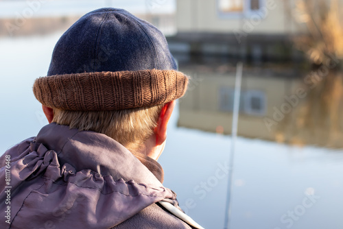 A white man fishing in a hat and jacket on a sunny day. Close-up rear view with blurred background.