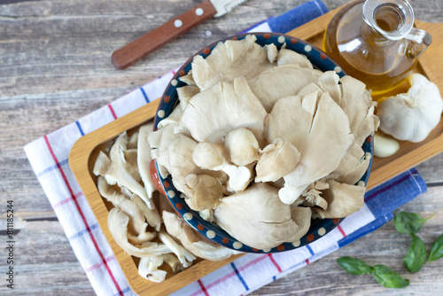 Raw oyster mushrooms (Pleurotus ostreatus) with olive oil, garlic, and basil leaves on wooden table. Top view. Fresh organic ingredients for healthy meal preparation.