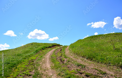 a green hill with a dirt road and a few clouds in the sky copy space