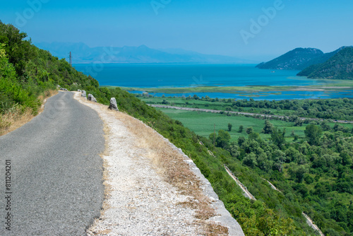 Narrow road near Skadar Lake with green and blue water. Beautiful summer landscape of mountains hills. Montenegro.