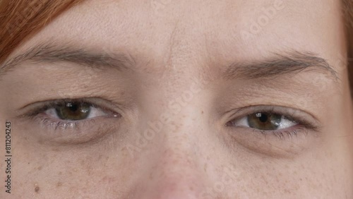 Brown female eyes close up. The red-haired girl looks at the camera and blinks frequently. Natural beauty without makeup. Drooping eyelid. High quality 4k footage