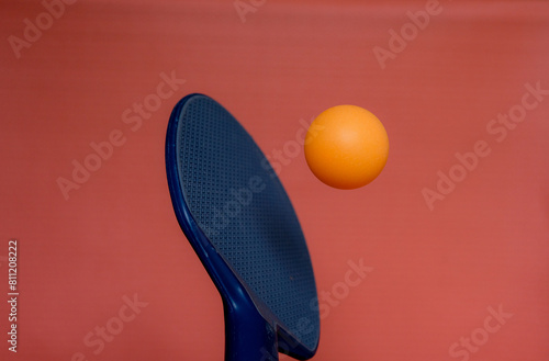 Blue table tennis bat. Orange table tennis ball. Movement. Pink background.