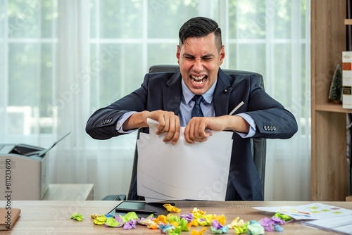 A businessman in a suit is ripping a piece of paper in frustration. photo