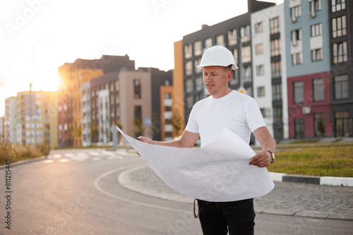 Successful engineer, architect, builder, businessman in hard hat, holds blueprint project on high rise residential buildings background. Construction concept. Verification and planning, real estate
