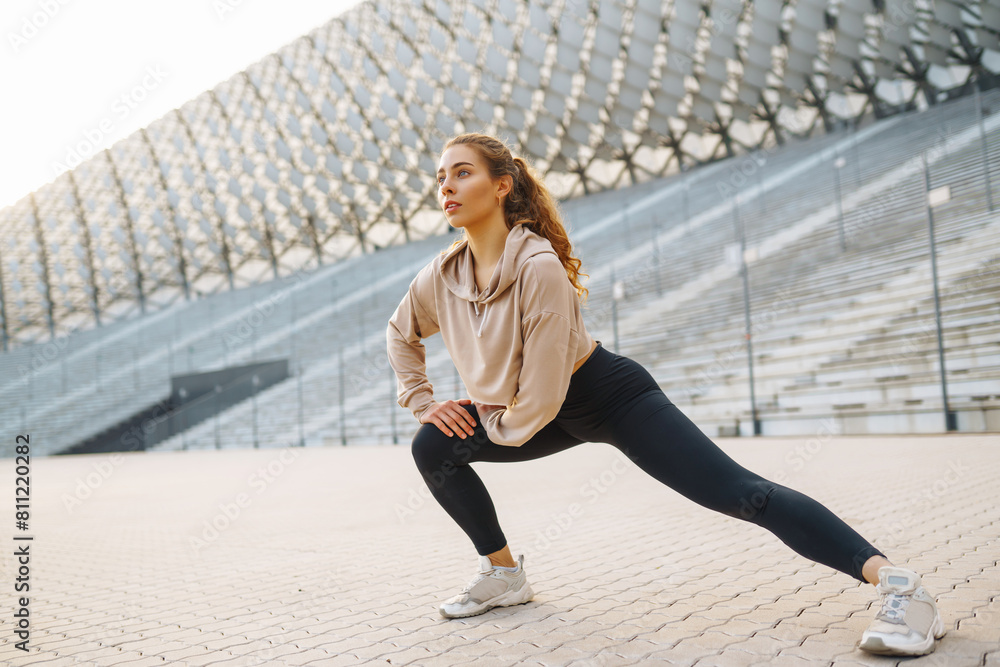 Fototapeta premium Smiling woman stretching her legs before jogging outdoors in the morning. Sport, gym and healthy body concept.