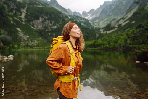 Woman traveler with yellow hiking backpack and hiking stiks enjoys the scenery. Active lifestyle. Wanderlust.
