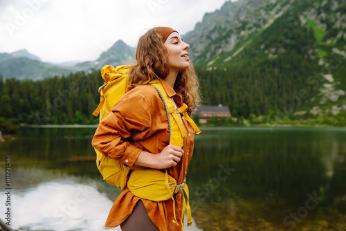 Woman traveler with yellow hiking backpack and hiking stiks enjoys the scenery. Active lifestyle. Wanderlust.