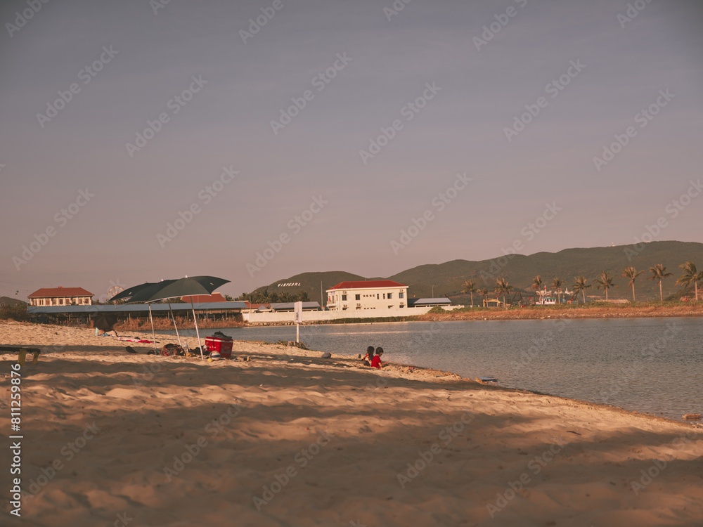 Sunny Beach Scene with People Relaxing on Sand and Colorful Kite Flying in Clear Blue Sky