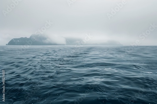 A large expanse of water with a solitary iceberg visible in the distance on a misty morning, A misty morning on the open ocean, with fog enveloping distant islands on the horizon photo