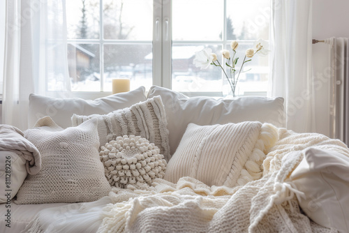 Scandinavian hygge home interior design of modern living room. Cozy white sofa with pillows and blanket against window.