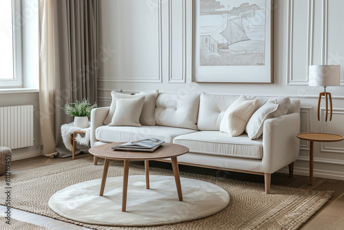 Round coffee table on beige rug near cozy sofa in room with classic paneling and poster. Scandinavian home interior design of modern living room. photo