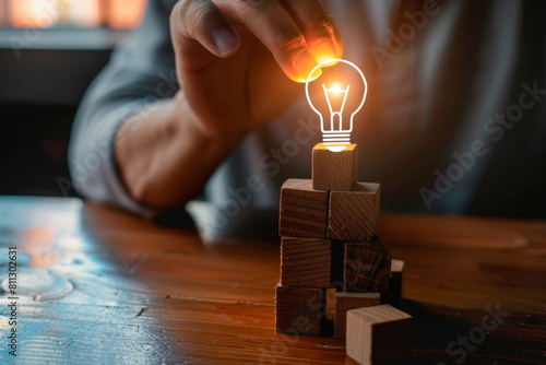 Wooden cubes with icons of head and light bulb on them, hand picking one cube from the top to make tower over wooden table background for ideas concept