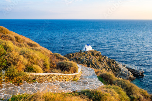Fototapeta Naklejka Na Ścianę i Meble -  Coastal path with steps to small church built on rocks and blue sea in background in Kastro village at sunrise, Sifnos island, Greece