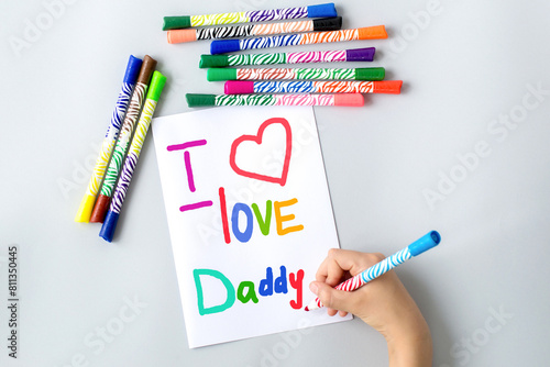 child draws with multi-colored felt-tip pens a poster gift card for dad for the holiday Father's Day with the text i love daddy and heart, sweet wish concept