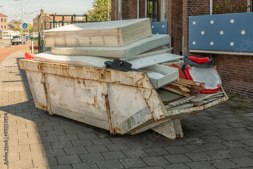 open steel industrial waste container filled with household waste and mattresses