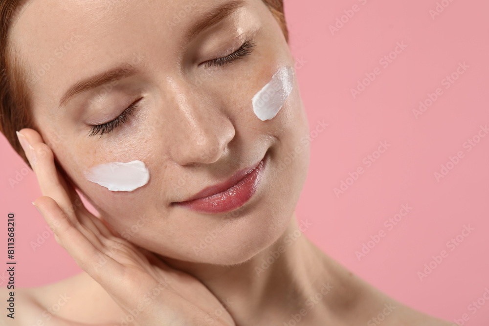 Obraz premium Beautiful woman with freckles and cream on her face against pink background, closeup. Space for text