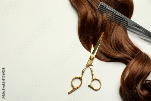 Professional hairdresser scissors and comb with brown hair strand on light grey background, flat lay. Space for text