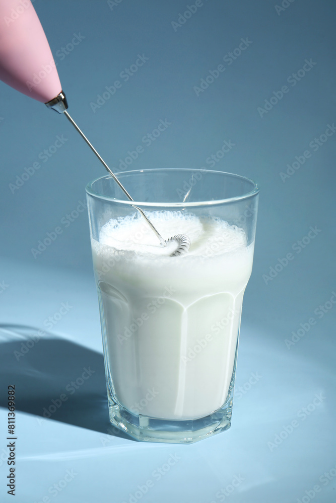 Whisking milk in glass with mini mixer (milk frother) on light blue background Whisking milk in glass with mini mixer (milk frother) on light blue background