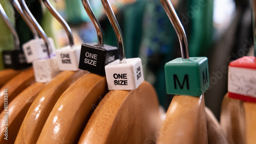 Close up of wooden clothes hangers with coloured size cubes for medium and one size in a retail fashion shop