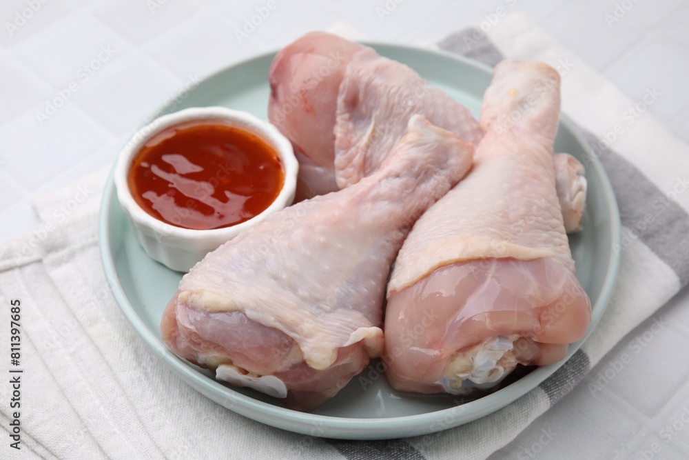 Fresh marinade and raw chicken drumsticks on white tiled table, closeup Fresh marinade and raw chicken drumsticks on white tiled table, closeup