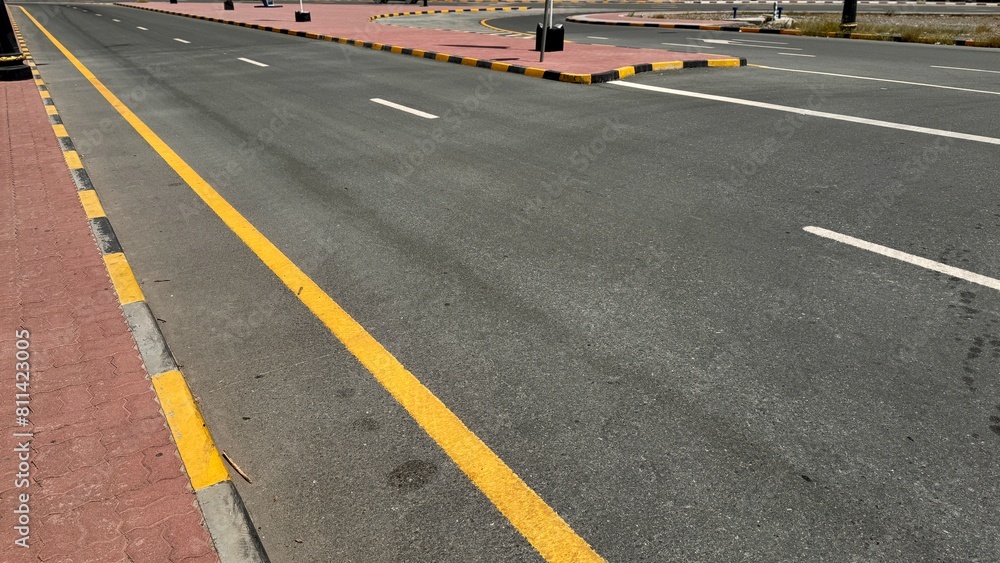 An empty curving auto road with distinct yellow restriction lines, white lane markings and a sidewalk edge An empty curving auto road with distinct yellow restriction lines, white lane markings and a sidewalk edge