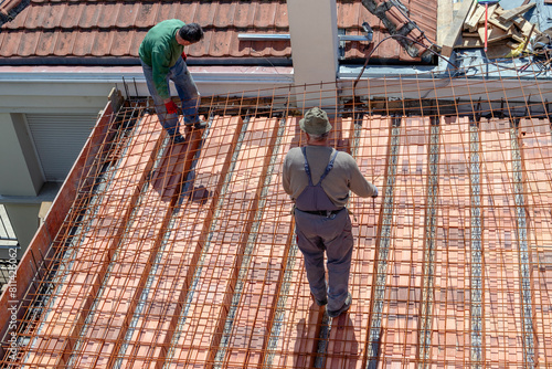 Construction workers prepare a steel mesh to reinforce a roof slab extension before pouring a concrete mix.