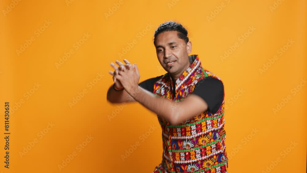 Radiant person having fun, dancing on oriental music, enjoying relaxation time. Joyous man doing entertaining bollywood dance moves, isolated over studio background, camera B Radiant person having fun, dancing on oriental music, enjoying relaxation time. Joyous man doing entertaining bollywood dance moves, isolated over studio background, camera B