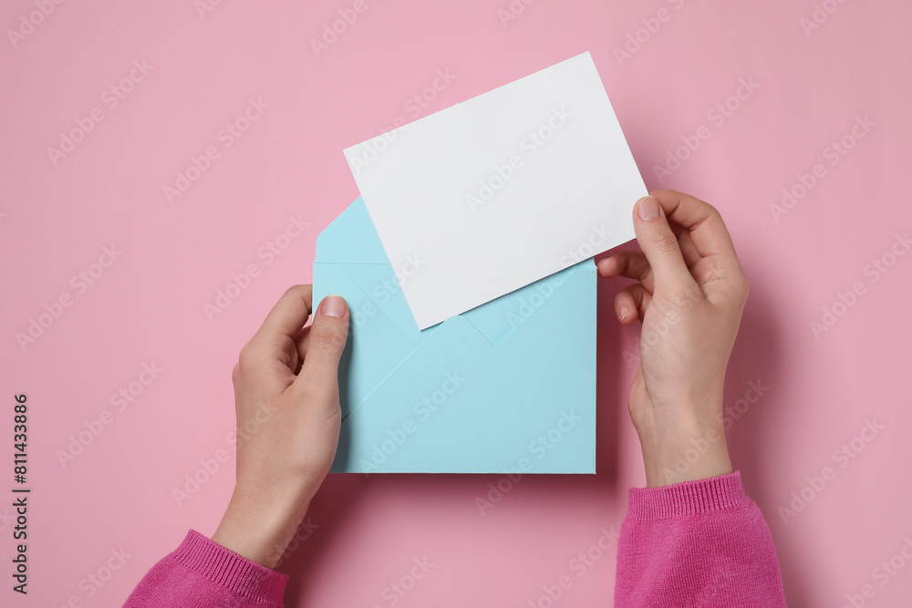 Woman taking card out of letter envelope at pink table, top view. Space for text Woman taking card out of letter envelope at pink table, top view. Space for text