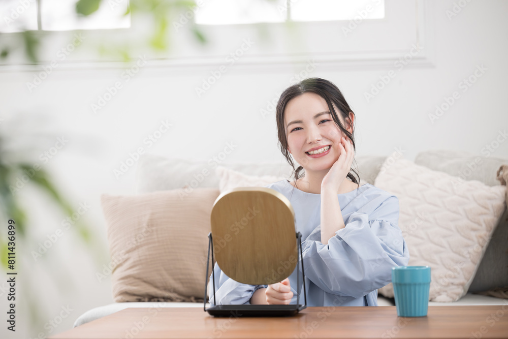 Young Asian (Japanese) woman with a pretty smile taking care of her skin in her room or living room, looking at the camera. Young Asian (Japanese) woman with a pretty smile taking care of her skin in her room or living room, looking at the camera.