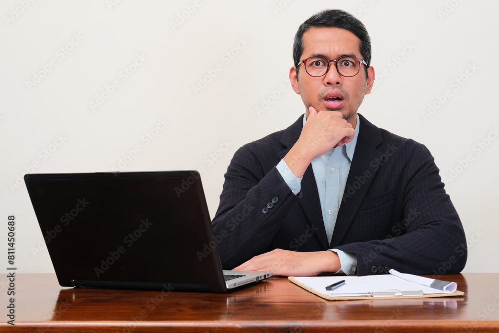 A manager sitting on his workplace looking camera with shocked expression A manager sitting on his workplace looking camera with shocked expression