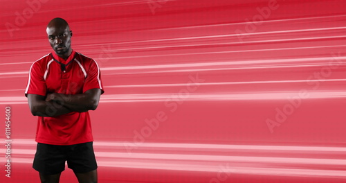 Image of rugby player standing with arms crossed over glowing red light trails background