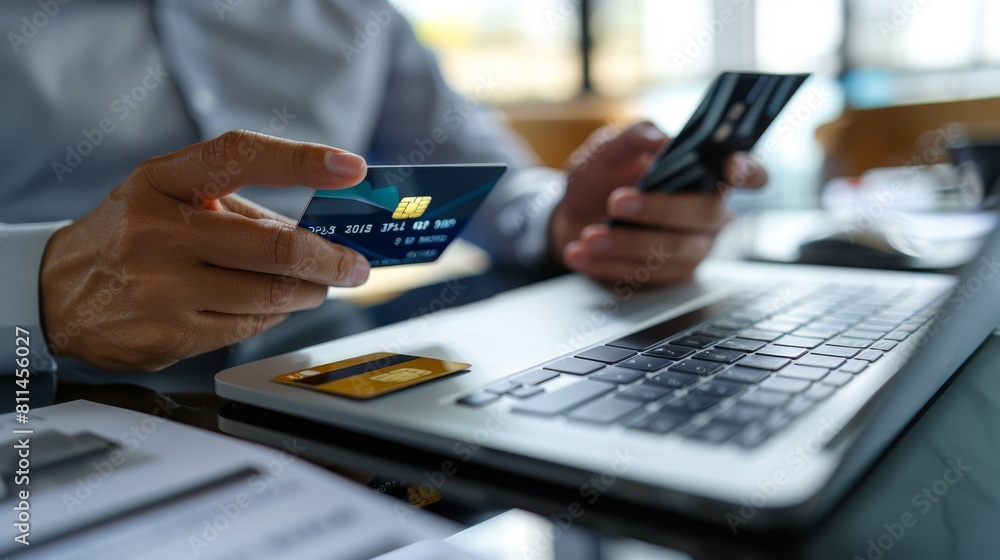 Closeup of hands holding a credit card and smartphone for online shopping, while sitting at home with a laptop computer on the desk Closeup of hands holding a credit card and smartphone for online shopping, while sitting at home with a laptop computer on the desk