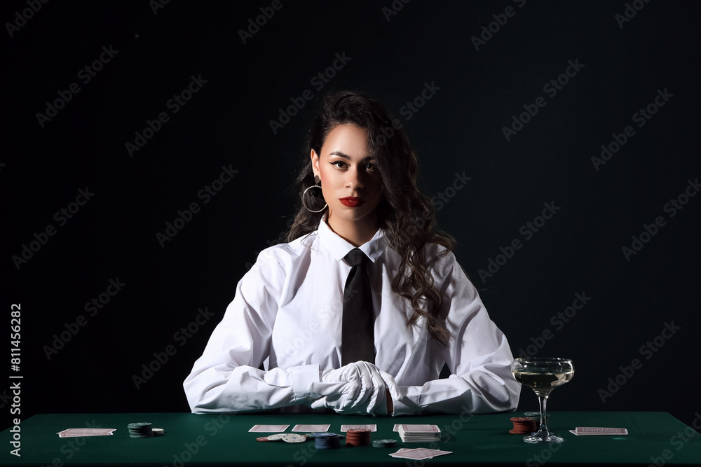 Beautiful African-American woman sitting at poker table with playing cards, chips and glass of champagne on black background Beautiful African-American woman sitting at poker table with playing cards, chips and glass of champagne on black background