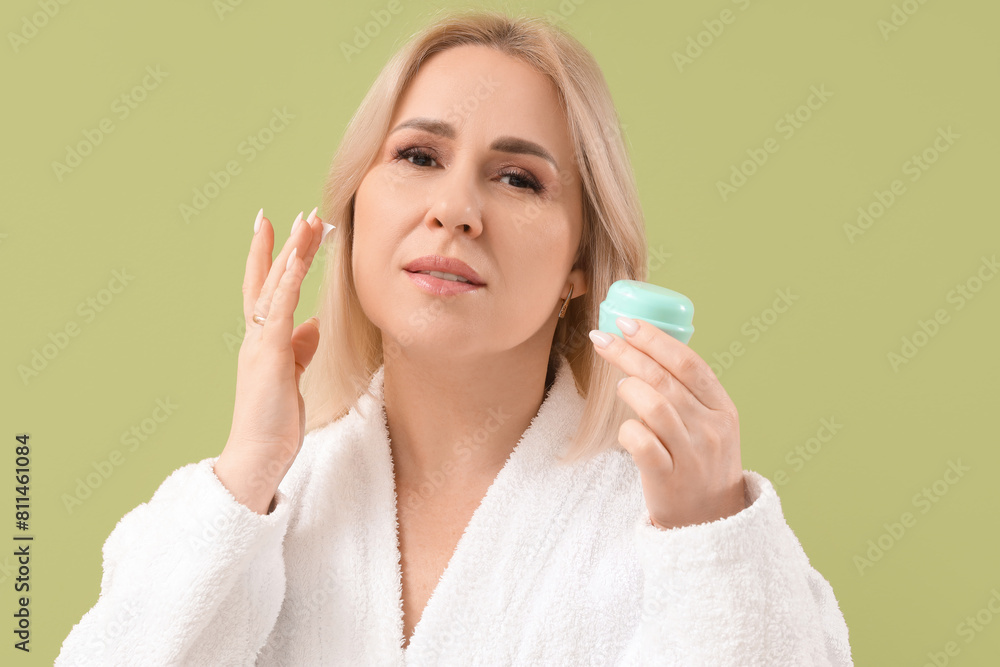 Beautiful mature woman in bathrobe with jar of cream on green background Beautiful mature woman in bathrobe with jar of cream on green background