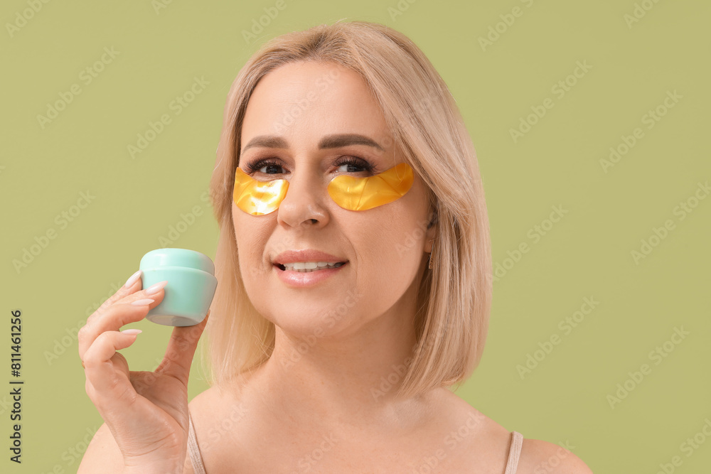 Beautiful mature happy woman with under-eye patches and jar of cream on green background Beautiful mature happy woman with under-eye patches and jar of cream on green background