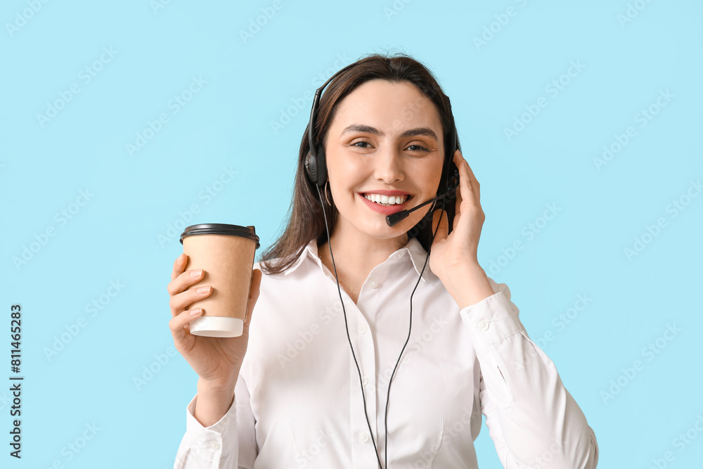 Female technical support agent in headset with paper cup of coffee on blue background Female technical support agent in headset with paper cup of coffee on blue background