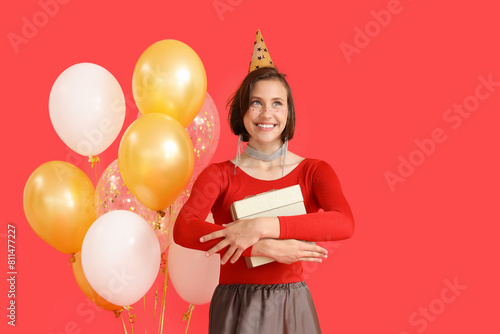 Beautiful woman in party hat with Birthday gift and balloons on red background