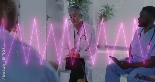 Image of heart rate monitor on caucasian female doctor discussing with healthworkers at hospital photo